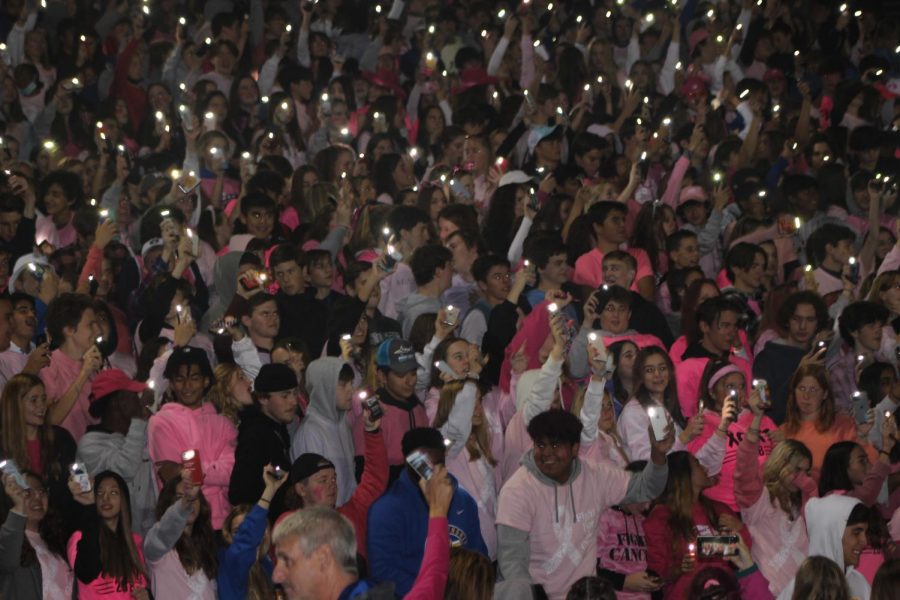 Students raise up phone flashlights at the LT Pink Out game (Burke/LION). 