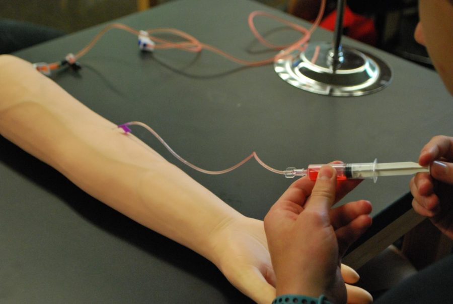 Maks Kazprzak 25 practices injecting with a needle in a dummy arm (photo courtesy of Caroline Gee 25).