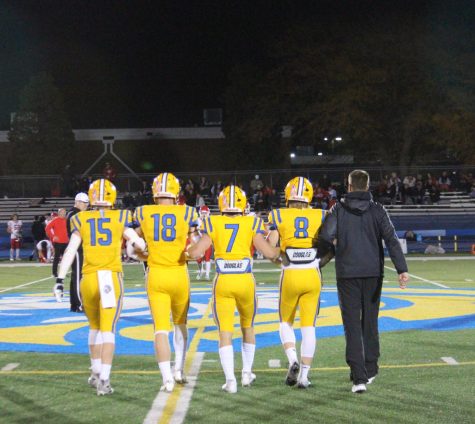 (Pictured from left to right) Cooper King ‘23, Graham Smith ‘23, James Georgelos ‘23, Danny Pasko ‘23, and Head Coach Jon Beutjer lock arms as they approach midfield for the coin toss before their first round matchup against Naperville Central (Klos/LION).