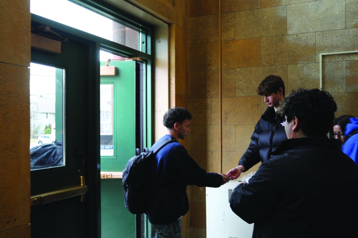 Sean Connolly ‘24 passes out Say Something Week wristband to student entering the building on March 7 in the NC Bell Tower Entrance, (LION/OBrien). 