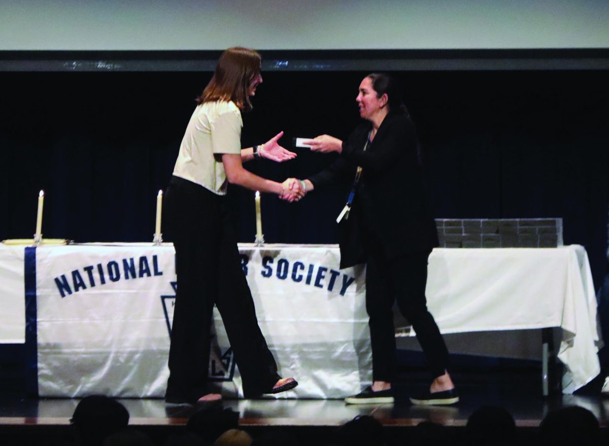 Student walks across stage and receives a membership certificate from Principal Jennifer Tyrell in front of friends and family at induction ceremony on April 17 in the NC Reber