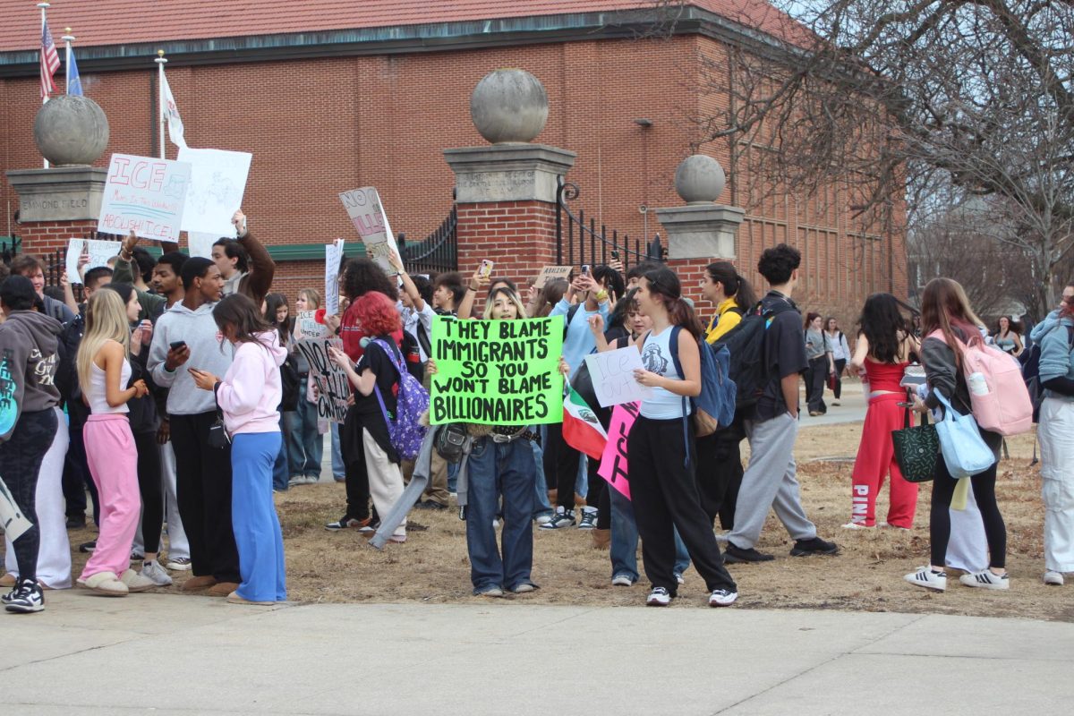 A student holds a sign that states “They blame immigrants so you won’t blame billionaires".